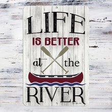 Load image into Gallery viewer, Detailed close-up of the Life Is Better at the River Metal Sign, showcasing vintage-style typography, crossed oars, and a classic canoe illustration on a weathered wood background.
