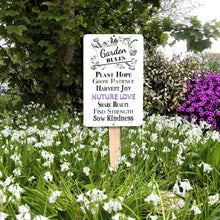 Load image into Gallery viewer, Garden Rules Nurture Love Metal Sign displayed in a flower garden setting with lush greenery and flowers.
