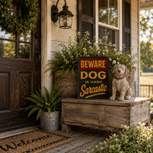 Load image into Gallery viewer, Funny Beware Dog sign displayed beside a farmhouse porch with a dog statue
