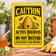 Load image into Gallery viewer, Caution Active Beehives metal sign displayed in an outdoor garden setting near beekeeping equipment and wooden garden accents.
