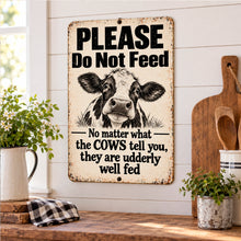 Load image into Gallery viewer, Funny cow Please Do Not Feed metal sign displayed in a rustic farmhouse kitchen with wood cutting boards and greenery
