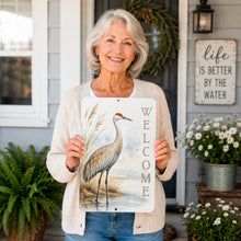 Load image into Gallery viewer, Woman holding a 'Welcome' sign with a crane design on a porch.
