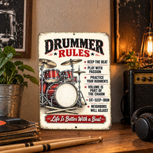 Load image into Gallery viewer, Vintage Drummer Rules metal sign displayed on a wooden surface with rustic music room decor, featuring a red drum set and playful drummer rules.
