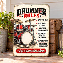 Load image into Gallery viewer, Vintage Drummer Rules aluminum sign leaning on a wooden music studio shelf beside drumsticks, headphones, a potted plant, and music equipment.
