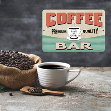 Load image into Gallery viewer, Rise and Grind Coffee Bar Metal Sign placed beside a rustic coffee setup with a steaming cup of coffee, burlap sacks filled with fresh beans, and a wooden coffee scoop, adding charm to any coffee bar.
