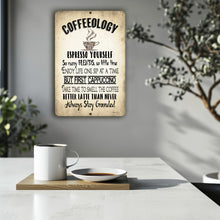 Load image into Gallery viewer, Coffeeology Metal Sign displayed in a modern, minimalist setting with a steaming coffee cup on a white table, adding a cozy yet stylish touch to coffee nook decor.
