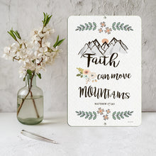 Load image into Gallery viewer, Faith Can Move Mountains Metal Sign displayed with white floral decor on a rustic wooden surface, creating a peaceful and inspiring ambiance.
