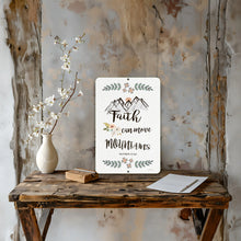 Load image into Gallery viewer, Faith Can Move Mountains Metal Sign displayed in a cozy rustic setting with a distressed wood backdrop and farmhouse-style decor.
