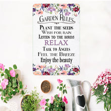 Load image into Gallery viewer, Dyenamic Art Garden Rules Metal Sign displayed in a garden setting with potted plants for a charming outdoor touch.
