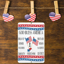 Load image into Gallery viewer, God Bless America Metal Sign – Displayed on a Rustic Wooden Surface with Hanging American Flag Heart Decorations, Creating a Warm and Patriotic Atmosphere.
