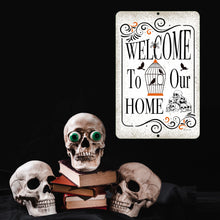 Load image into Gallery viewer, Halloween Welcome Home Metal Sign displayed with eerie skull decorations, black books, and green-glowing eyes for a haunting effect.
