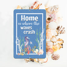Load image into Gallery viewer, Coastal-inspired setting featuring the Dyenamic Art Home Is Where the Waves Crash Metal Sign, styled with nautical accents, seashells, and beach-themed decor.
