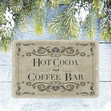 Load image into Gallery viewer, Hot Cocoa &amp; Coffee Bar Metal Sign placed on a snowy wooden background with frosted pine branches, adding a cozy winter theme to seasonal kitchen decor and holiday beverage stations.
