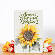 Load image into Gallery viewer, Dyenamic Art Love The Life You Live Sunflower Metal Sign with fresh flowers, creating a cozy and cheerful aesthetic.
