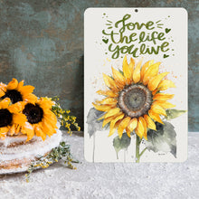 Load image into Gallery viewer, Dyenamic Art Love The Life You Live Sunflower Metal Sign placed near a rustic cake with sunflowers, adding charm to kitchen decor.
