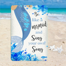 Load image into Gallery viewer, Dyenamic Art 'Be Like a Mermaid and Sing Your Own Song' metal sign placed on a sandy beach with seashells and starfish, enhancing its ocean-inspired theme.
