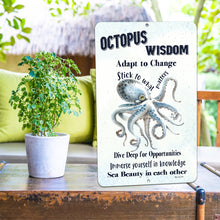Load image into Gallery viewer, The Octopus Wisdom Metal Sign displayed in a relaxed outdoor setting, paired with tropical decor, adding a touch of nautical charm to a patio or beach-themed space.

