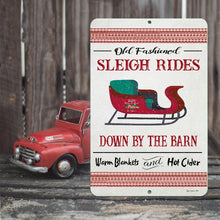Load image into Gallery viewer, Old Fashioned Sleigh Rides Metal Sign displayed on a rustic wooden surface with a vintage red truck, capturing a farmhouse holiday aesthetic.
