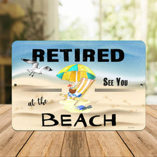 Load image into Gallery viewer, Dyenamic Art - Retired at the Beach Metal Sign – A Coastal Retirement Sign Displayed on a Rustic Wooden Table with Soft Natural Light. A Charming Addition to Any Beach House, Patio, or Outdoor Space.
