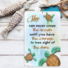 Load image into Gallery viewer, Beach-inspired setting with the Dyenamic Art Sea Turtle Crossing Metal Sign placed on a rustic wooden surface, surrounded by nautical decor, starfish, and seashells—perfect for coastal home aesthetics.
