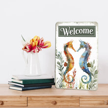Load image into Gallery viewer, Dyenamic Art Seahorse Welcome Sign elegantly placed on a modern wooden console table, complementing a stylish interior with fresh flowers and stacked books.
