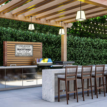 Load image into Gallery viewer, The Backyard Bar and Grill Metal Sign displayed in an outdoor kitchen setup with a wooden pergola, modern countertops, and string lights. A stylish addition for entertaining spaces.
