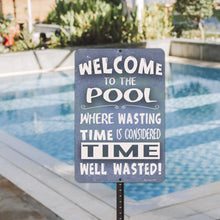 Load image into Gallery viewer, Dyenamic Art Welcome to the Pool Metal Sign displayed near a swimming pool with sparkling blue water, adding a fun and inviting touch to any poolside setting.

