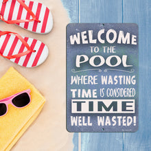Load image into Gallery viewer, Welcome to the Pool Metal Sign by Dyenamic Art, styled on a sandy and wooden background with summer essentials like striped flip-flops, sunglasses, and a yellow towel. Perfect for beach and pool lovers.
