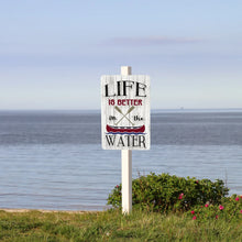 Load image into Gallery viewer, Life Is Better On the Water metal canoe sign mounted on a white post near a peaceful lakeshore with blue sky
