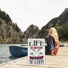 Load image into Gallery viewer, Decorative metal canoe sign on a dock with woman sitting beside boats and scenic mountain lake in the background.
