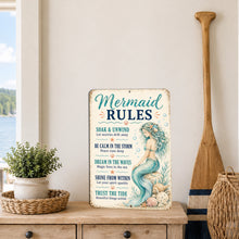 Load image into Gallery viewer, A decorative rectangular sign with a vintage-style mermaid illustration and the text 'Mermaid Rules' is displayed on a wooden table in a coastal-themed room setting with a paddle, basket, and potted plant.
