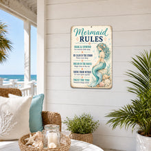 Load image into Gallery viewer, A decorative rectangular wall sign with a distressed vintage look hangs on a white shiplap wall in a coastal porch setting. The sign reads 'Mermaid RULES' with a mermaid illustration and text including 'Soak &amp; unwind', 'Be calm in the storm', and 'Dream in the waves'.
