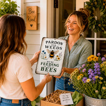 Load image into Gallery viewer, Woman holding Pardon the Weeds Feeding Bees metal sign in colorful flower garden with cottagecore outdoor decor styling
