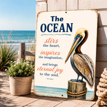 Load image into Gallery viewer, Pelican wall decor sign for beach house featuring The Ocean Stirs the Heart quote, coastal metal sign, nautical wall art, ocean lover gift outdoor setting

