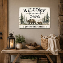 Load image into Gallery viewer, A rustic metal sign mounted on a beige wall above a wooden console table. The sign reads 'WELCOME to our neck of the Woods Johnson Family' with an illustration of a bear and pine trees.
