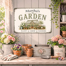 Load image into Gallery viewer, A decorative custom metal sign reading "Martha's GARDEN" with an illustration of a greenhouse and plants, displayed on a rustic wooden table in a styled garden room scene with flowers, pots, gloves, and gardening tools.
