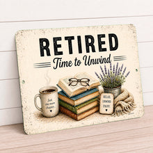 Load image into Gallery viewer, Retired Time to Unwind metal wall sign displayed in cozy farmhouse reading nook with warm neutral decor
