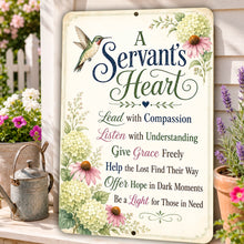 Load image into Gallery viewer, A decorative rectangular sign with rounded corners featuring the phrase “A Servant’s Heart” in large script and serif text, surrounded by floral illustrations and a hummingbird. The sign is shown outdoors leaning against a white wooden post beside a galvanized watering can and potted flowers.
