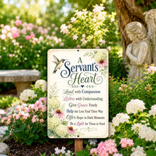 Load image into Gallery viewer, A decorative garden sign with floral illustrations and the text 'A Servant's Heart' and a prayer, displayed in a sunny garden with flowers, a bench, and a stone angel statue in the background.
