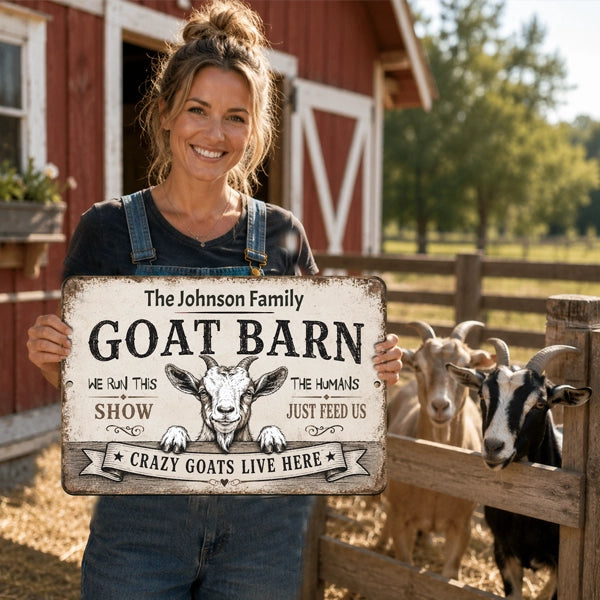 Woman holding personalized Goat Barn metal sign with goats beside a rustic red barn
