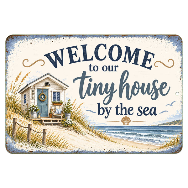 Welcome to Our Tiny House by the Sea metal sign featuring a coastal cottage, blue door, sandy dunes, ocean waves, and weathered blue border on white background.