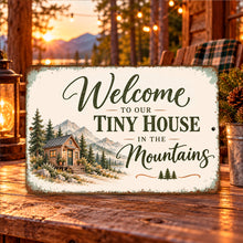 Load image into Gallery viewer, Vintage-style tiny house metal welcome sign displayed in a warmly lit mountain cabin setting with natural wood accents and scenic outdoor surroundings.

