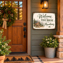 Load image into Gallery viewer, Mountain tiny home welcome sign hanging beside a wooden cabin entrance with a porch lantern, rustic door, and potted plants.
