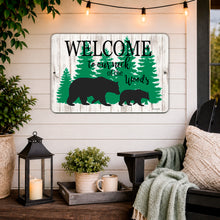 Load image into Gallery viewer, Welcome to Our Neck of the Woods rustic cabin sign with black bear and cub, displayed on a cozy farmhouse porch with pine trees and weathered wood background.

