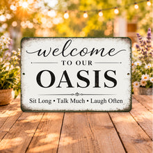 Load image into Gallery viewer, Decorative sign with 'Welcome to our Oasis' text on a wooden surface with plants and lights in the background.
