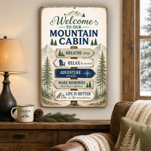 Load image into Gallery viewer, Welcome To Our Mountain Cabin metal decorative sign with mountain cabin theme on a wall above a wooden table with a lamp and mug
