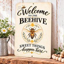 Load image into Gallery viewer, Vintage beehive welcome sign leaning against a light wall on a wooden surface with decorative plants and warm neutral farmhouse accents.
