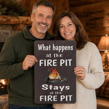 Load image into Gallery viewer, A smiling couple stands indoors holding a dark rectangular sign that reads, 'What happens at the FIRE PIT Stays at the FIRE PIT,' with a small campfire graphic in the center. The room has warm wood walls and a lamp in the background.
